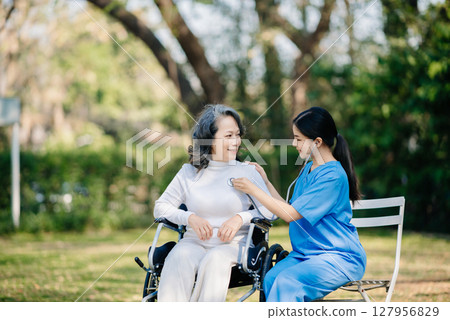 Elderly asian senior woman on wheelchair with Asian careful caregiver. Nursing home hospital garden Elderly asian senior woman on wheelchair with Asian careful caregiver. Nursing home hospital garden 127956829