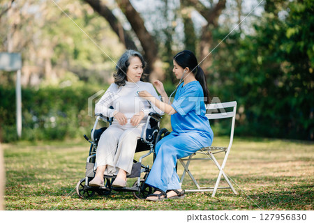 Elderly asian senior woman on wheelchair with Asian careful caregiver. Nursing home hospital garden Elderly asian senior woman on wheelchair with Asian careful caregiver. Nursing home hospital garden 127956830