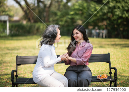 Happy adult granddaughter and senior grandmother having fun enjoying talk sit in garden with green nature. 127956900
