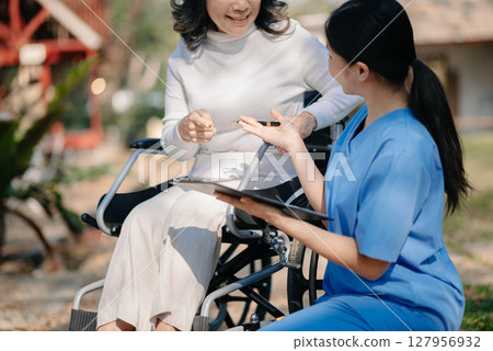 Elderly asian senior woman on wheelchair with careful caregiver and encourage patient, walking in garden. with care from a caregiver and senior health insurance. 127956932