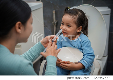 mother making nasal wash for happy toddler girl with syringe and saline. cleaning nose 127957552