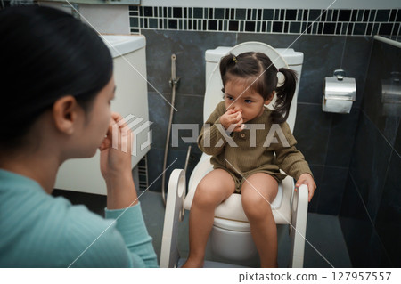 mother is helping toddler girl use the toilet. potty training and learning in bathroom mother is helping toddler girl use the toilet. potty training and learning in bathroom 127957557