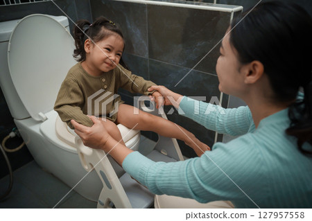 mother is helping toddler girl use the toilet. potty training and learning in bathroom 127957558