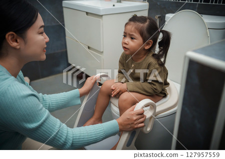 mother is helping toddler girl use the toilet. potty training and learning in bathroom 127957559