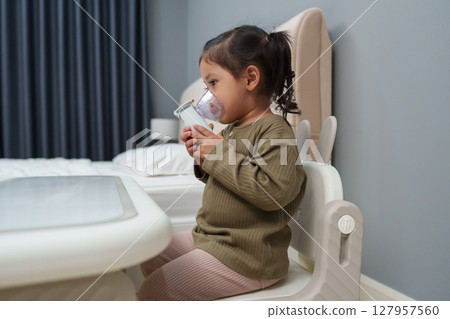 toddler girl making inhalation treatment with nebulizer at home 127957560