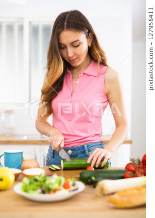 Woman cook reads the recipe in laptop and cooks salad in kitchen Woman cook reads the recipe in laptop and cooks salad in kitchen 127958411