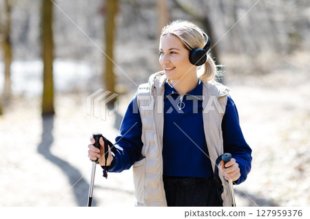 Young Woman Nordic Walking in Forest Listening Music with Headphones Young Woman Nordic Walking in Forest Listening Music with Headphones 127959376