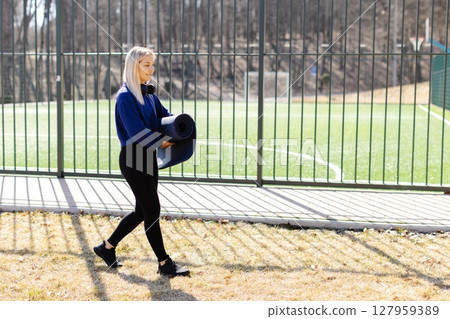 Young woman carrying yoga mat walking near sports field 127959389