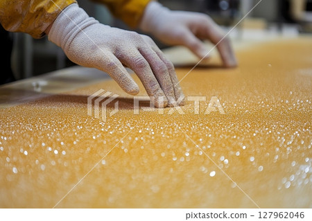 Close-up of a gloved hand touching a golden, granular surface, showcasing texture and detail 127962046