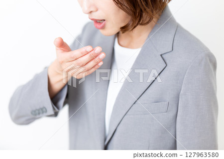 A middle-aged woman in a suit checking her bad breath 127963580