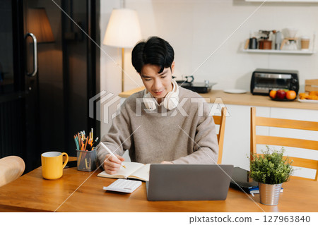 Lifestyle people, using laptop computer and smartphone sitting in the kitchen. Happy male, entrepreneur, small business owner working online at home office. 127963840