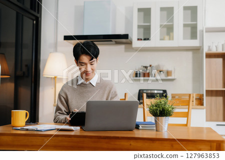 Lifestyle people, using laptop computer and smartphone sitting in the kitchen. Happy male, entrepreneur, small business owner working online at home office. Lifestyle people, using laptop computer and smartphone sitting in the kitchen. Happy male, entrepreneur, small business owner working online at home office. 127963853