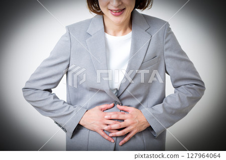 A middle-aged woman in a suit suffering from stomach pain 127964064