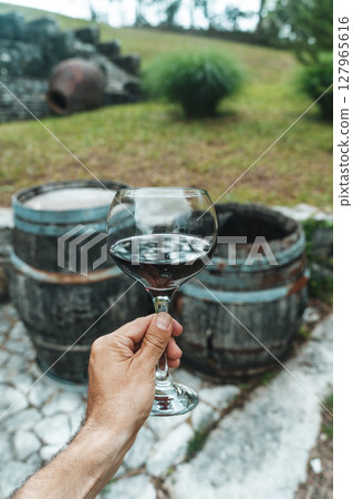 Red Wine Glass in Hand with Stone Cellar Background in France or Italy 127965616