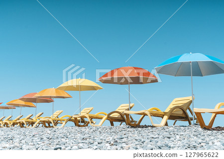 Colorful Beach Umbrellas and Sun Loungers on a Pebble Seaside Colorful Beach Umbrellas and Sun Loungers on a Pebble Seaside 127965622