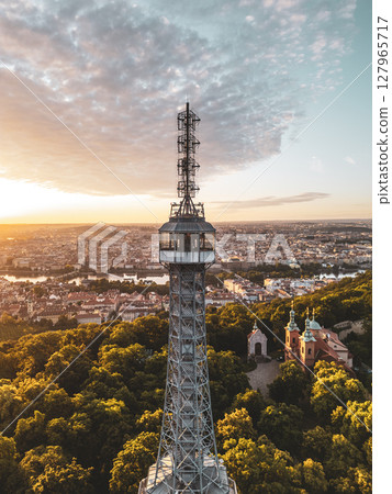 Petrin Lookout Tower rises above the lush greenery of the park, capturing the stunning colors of sunrise over the city of Prague. The beautiful skyline unfolds in the early morning light. Petrin Lookout Tower rises above the lush greenery of the park, capturing the stunning colors of sunrise over the city of Prague. The beautiful skyline unfolds in the early morning light. 127965717