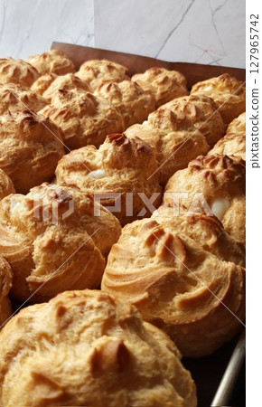 Light, airy cream puffs filled with luscious vanilla custard, dusted with powdered sugar. A delightful treat that melts in your mouth with each bite, perfect for any occasion. 127965742