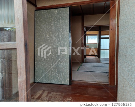 從後門看到的一棟老房子，前景是玻璃門和損壞的地板，背景是一扇翻轉滑動門和捆紮的電纜 127966185