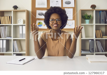 Portrait african american woman sitting at office desk with raised palms Portrait african american woman sitting at office desk with raised palms 127966317