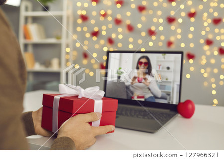 Close up of red gift box in male hands in front of laptop screen during online date. 127966321
