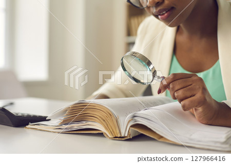 African american woman skeptically looking via magnifying glass at document 127966416