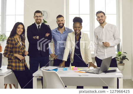 Team of happy young diverse business people standing in modern office and smiling Team of happy young diverse business people standing in modern office and smiling 127966425