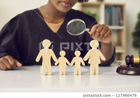 Young african american judge with magnifying glass looking on family wood figure 127966476