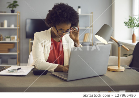 Young african american woman carefully reads text on laptop screen in office Young african american woman carefully reads text on laptop screen in office 127966480