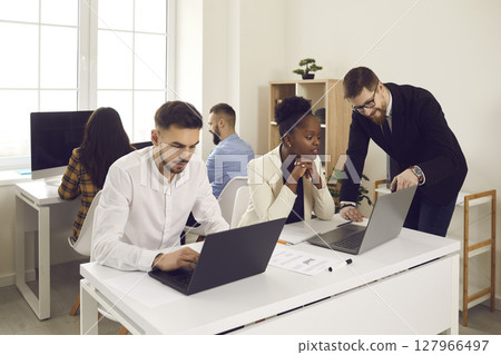 Confident businessman talking checking afro american employee report on laptop Confident businessman talking checking afro american employee report on laptop 127966497