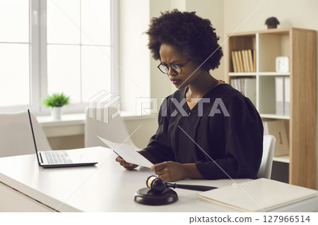 Frowning african american female judge reading legal paper document at desk 127966514