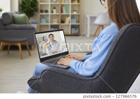 Woman sitting in chair with laptop and having video conference with online doctor 127966576
