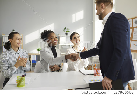 Young multiracial business team shakes hands with a man welcoming him as a new team member. 127966593