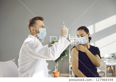 Doctor in medical face mask preparing syringe before giving injection to patient Doctor in medical face mask preparing syringe before giving injection to patient 127966594