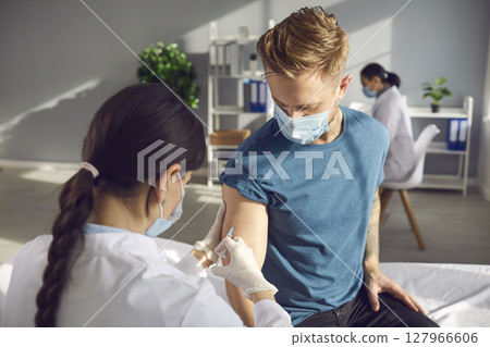 Man in medical face mask getting COVID-19 vaccine in sunny office of modern clinic Man in medical face mask getting COVID-19 vaccine in sunny office of modern clinic 127966606