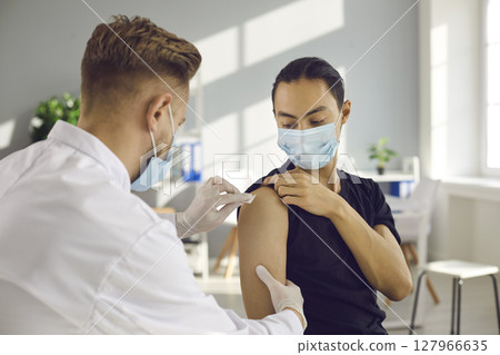 Young man in medical face mask getting seasonal flu shot or modern Covid-19 vaccine 127966635