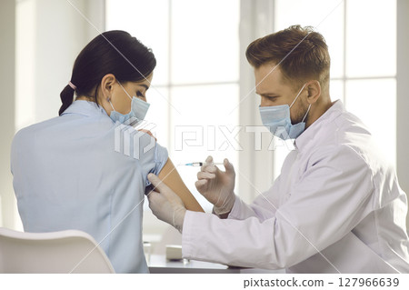 Man doctor reaching with syringe for woman patient arm for making vaccination Man doctor reaching with syringe for woman patient arm for making vaccination 127966639