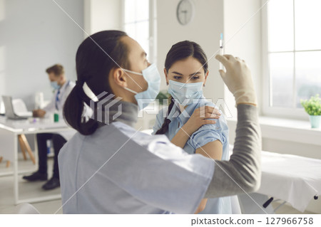 Young woman in medical face mask getting Covid-19 clinical trial vaccine at hospital 127966758