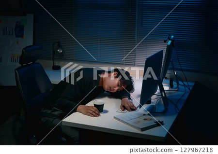 Exhausted businessman falling asleep at his desk under dim blue lighting 127967218