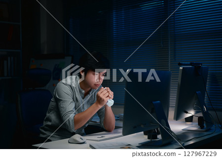 Tired man gripping a crumpled paper, sitting in the office and tackling important tasks after hours 127967229