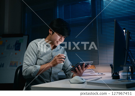 Focused office worker reviewing documents while working late into the night Focused office worker reviewing documents while working late into the night 127967451