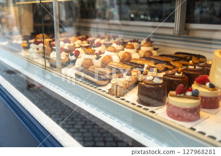 Glass display of a French patisserie showcasing various gourmet pastries including eclairs, tarts 127968281