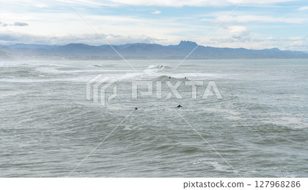Surfers in wetsuits wait for waves in the cold Atlantic Ocean near Biarritz, France 127968286