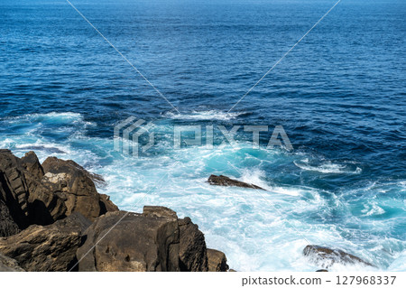 Wave impact exposes basalt layers and erosion patterns 127968337