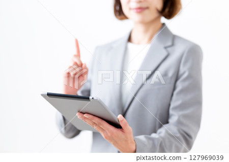 一位身穿灰色西裝的中年女子拿著平板電腦,食指向上 一位身穿灰色西裝的中年女子拿著平板電腦,食指向上 127969039