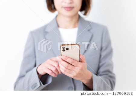 A middle-aged woman in a gray suit holding a smartphone 127969198