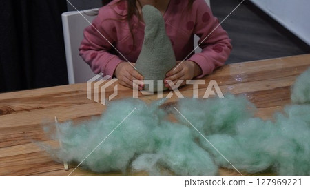 Kid girl hands stuffing handcrafted felt toy using green sintepon cotton filling 127969221