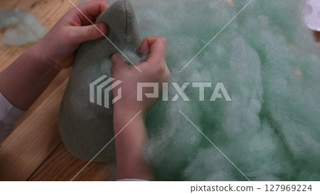 Kid hands make stuffed toy using sintepon hollow cotton filling 127969224
