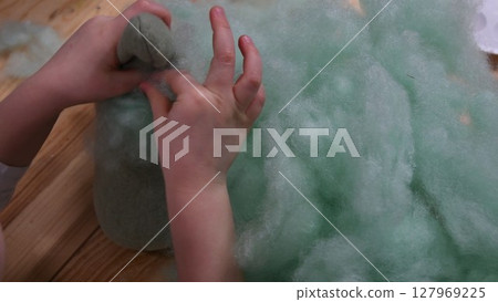 Kid hands make stuffed toy using sintepon hollow cotton filling 127969225