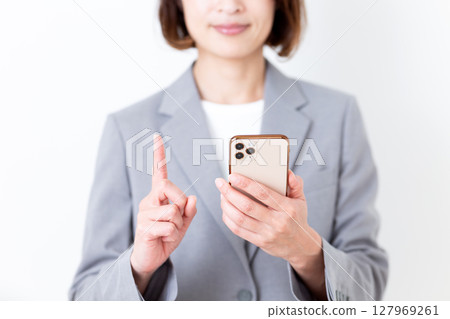 一位身穿灰色西裝的中年女子拿著智慧型手機，食指向上 127969261