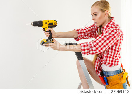 Woman using drill on ladder 127969340